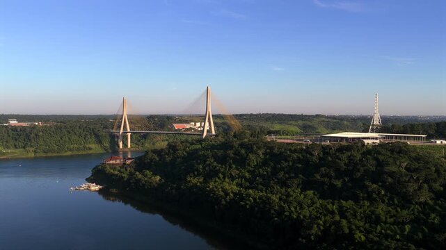 The bridge stretches across verdant landscapes under clear skies, connecting Paraguay and Brazil. Ideal for use in geographic or cultural documentaries.