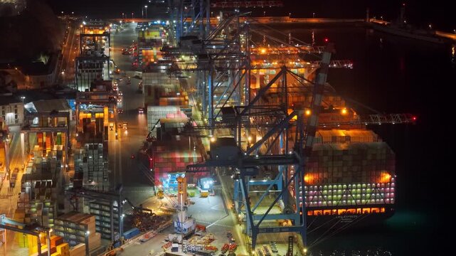 Aerial orbit establishing a giant cargo ship being unloaded, loaded with shipping containers; unloading operations at the Port of Valparaiso at night, Chile