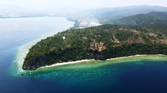 Aerial drone shots of lush forested peninsulas meeting calm turquoise bays and sandy white beaches in Glan, Sarangani, Philippines, highlighting serene island coastline beauty.