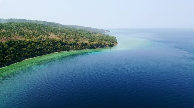 Scenic views of lush green vegetation meeting serene blue and turquoise ocean waters along the island coastline of Glan, Sarangani, Philippines, under clear, bright skies.