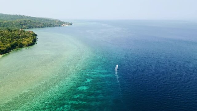 A speedboat cutting through clear turquoise and deep blue waters along the tropical coastline of Glan, Sarangani, Philippines, leaving a distinctive white wake.