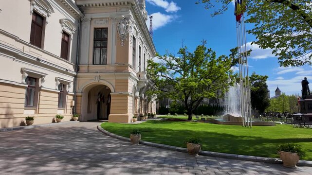 Slow motion view of Iasi City Hall courtyard on Stefan cel Mare with tree, fountain and flags in a sunny day