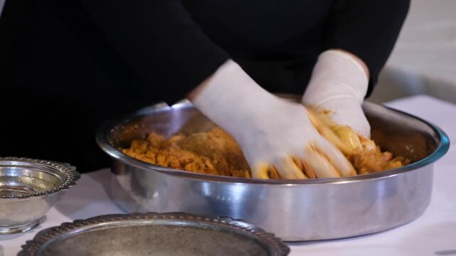 Close-up of gloved hands kneading kibbeh dough in a metal bowl, highlighting traditional Middle Eastern food preparation, texture, spices, and hygienic cooking process in kitchen.