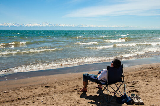 man is sitting on the camp chair on the beach