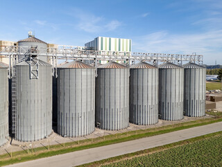 Fototapeta premium Grain silos stand tall in a storage facility surrounded by fields. This aerial view shows their structure and layout.