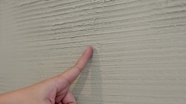 Person Touching a Rough Grey Textured Concrete Wall with Index Finger