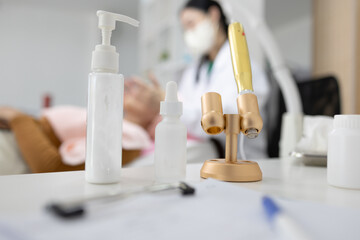 Medical professional wears mask while attending to patient. White pump bottle stands beside small vials and tools. Golden stand holds precision instruments nearby  © Pattra