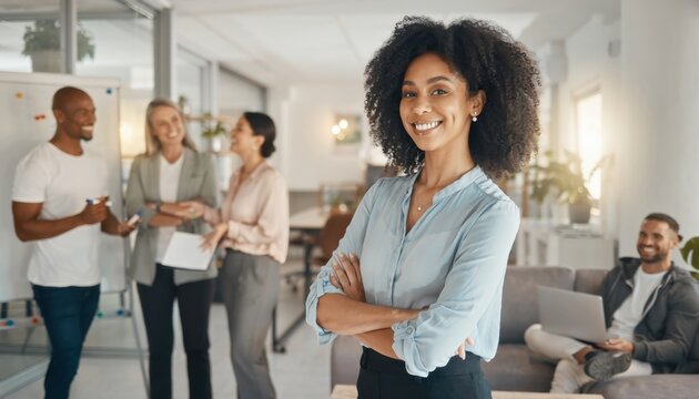 Confident Leader in Modern Office: A poised woman exudes confidence and charisma, with arms crossed in front of a modern office, as colleagues engage in discussions in the background.