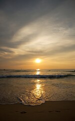 Fototapeta premium Scenic golden sunset over tropical beach with gentle ocean waves and glowing sun reflections on the sand