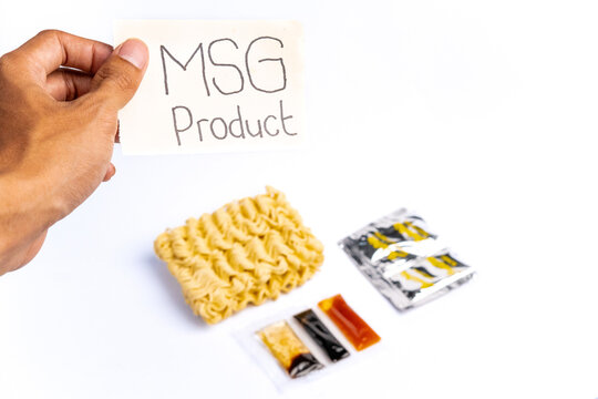Hand holding MSG Product sign over dry instant noodle block with seasoning sachets isolated on white background
