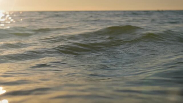 Close view of ocean water surface at golden hour with soft waves and sunlight reflections, creating peaceful natural texture ideal for relaxation, travel, wellness or environmental visual content