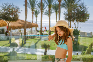 Obraz premium Young girl in a straw hat on a glass balcony looking at the camera in a tropical resort