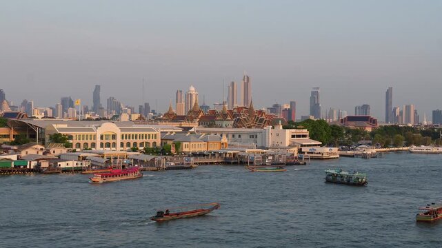 Bangkok, Thailand: Boats and ferry in front of famous Grand Palace with Wat Phra Kaew on the Chao Praya river in the heart of Bangkok, Thailand capital city with city skyline in the back