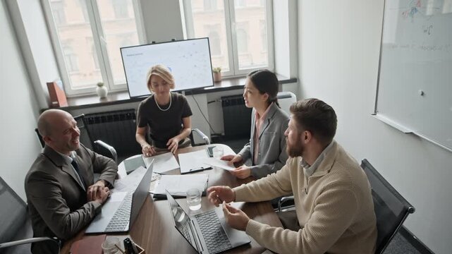 High angle shot of business team sitting at table and discussing new startup, sharing opinions and emotions