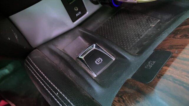hand pressing handbrake button close-up shot on car center console with finger activating electronic parking brake, driving scene showing vehicle control and safety system usage in interior