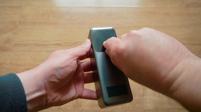 Hands removing protective film from new power bank close up portable charger. Person preparing external battery pack indoor minimal tech lifestyle. Mobile charging accessory startup scratch peel
