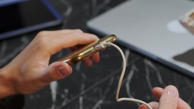 hand inserting charging cable close-up shot into phone port, device charging process showing power connection and energy supply for mobile device in everyday usage environment