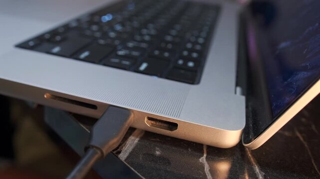 hand inserting usb-c cable close-up shot into laptop port, device connection process showing power and data transfer setup with modern interface in workspace environment