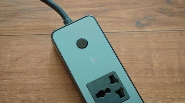 Switching portable power strip on and off using button with right and left hands alternately. Finger pressing control button on extension socket activating and deactivating electricity flow. Power