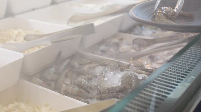 Customer Using Tongs to Pick Fresh Raw Shrimp at Buffet Restaurant