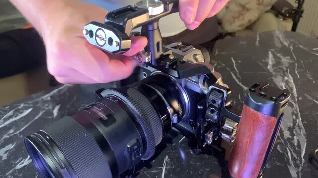 Hands installing handle on camera cage close-up, attaching top grip to rig system for improved control and stability, preparing filming equipment for handheld shooting, technical setup in videography