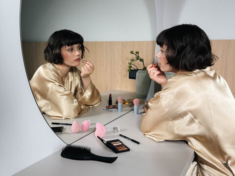 Young woman in silk robe doing everyday makeup at cosmetic vanity