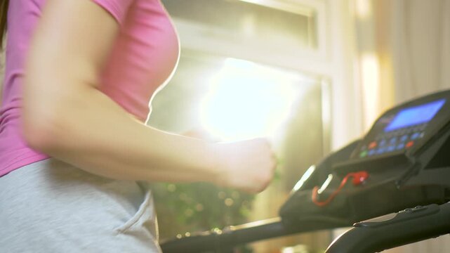 Fitness routine of unrecognizable woman jogging on treadmill with control console in apartment interior. Steady cardio training during daily home workout and endurance running session. Active