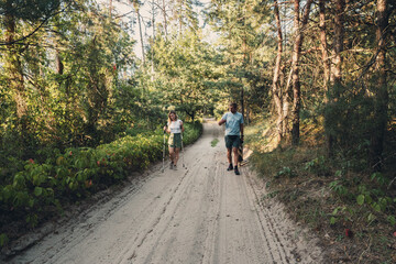 Obraz premium Couple hiking on a sandy forest road with Nordic walking poles on a sunny day