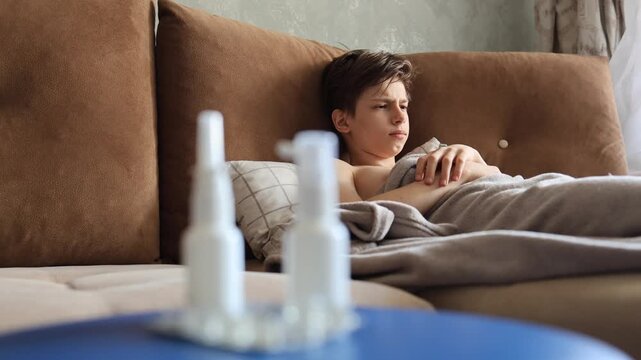 sick man lying in bed suffering virus having medicine tablets. drinking pill. A sick teenager lies on the couch, coughing and taking pills for a seasonal virus.