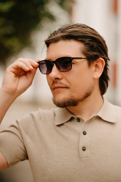 Confident Man Adjusting Sunglasses Outdoors, Polo Shirt, Tiedback Hair, Leather Watch Startup Founder Pausing