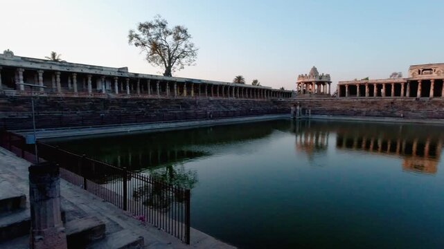 Slow panning shot of historic stepped Kalyani pond, stone corridors, Bhuvaneshwari Mantapa Dome and Yoga Narasimha Swamy Temple at sunset, Melukote Karnataka