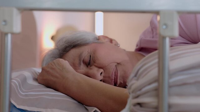 Elderly senior woman sleeping on comfortable hospital bed resting quiet calm and peaceful during illness recovery receiving necessary medical care treatment at nursing facility