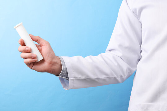 Doctor in a white medical coat holding rectal suppositories on a blue background