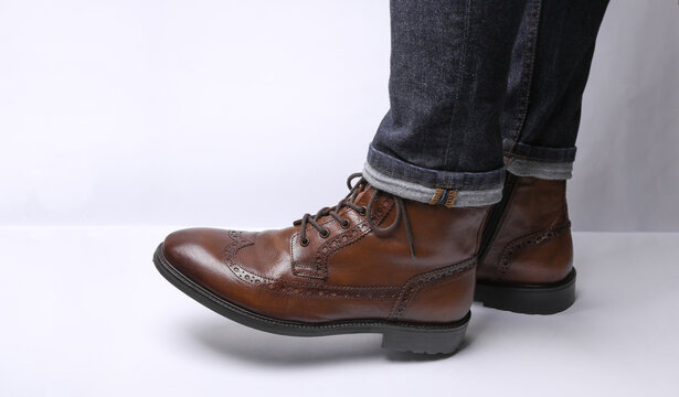 Male legs in jeans and classic leather brogue boots on a white background