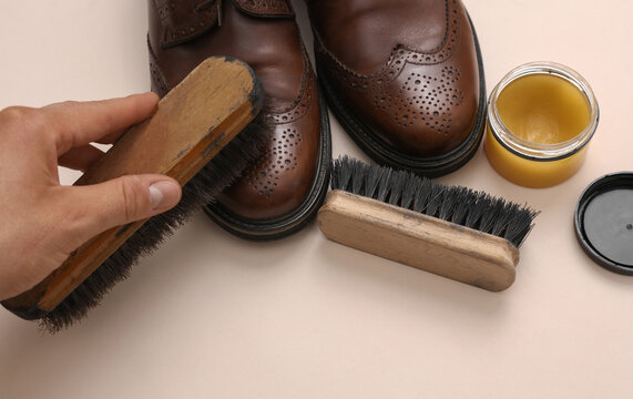Man's hand takes care of leather shoes on a beige background