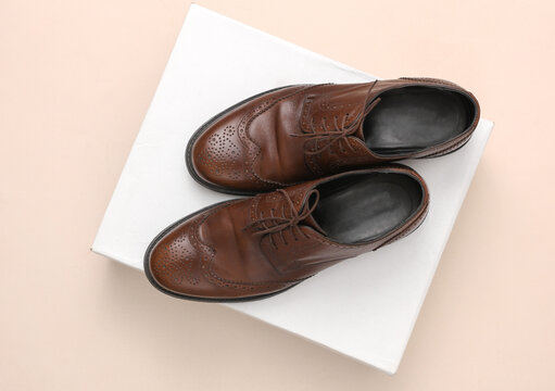 Man's Classic leather brown brogue shoes and box on a beige background. Top view