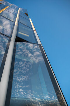Blue sky reflections on modern building glass facade with minimal architecture and sharp angle creating clean exterior background with windows