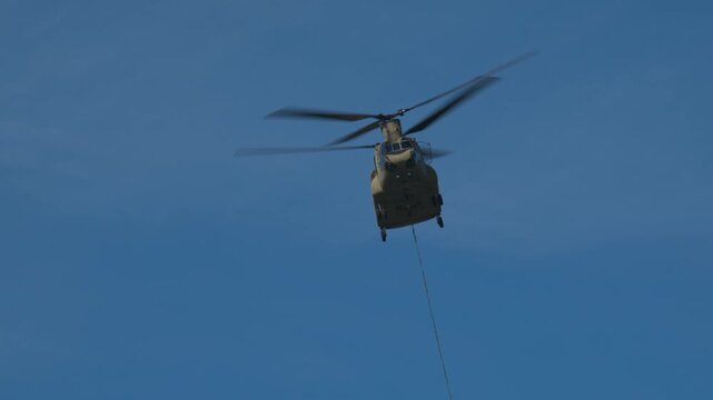 Transport helicopter of Dutch Royal Air Force carrying a water bucket for extinguishing wildfires in nature.