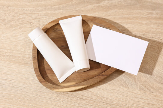 White blank crem tubes with white blank business card in a wooden tray. Beauty concept