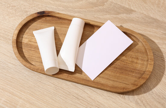 White blank crem tubes with white blank business card in a wooden tray. Beauty concept