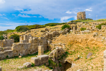 Fototapeta premium Sunny view of Tharros Archaeological Area on Capo San Marco Cape with Torre di San Giovanni di Sinis Tower in the background, Sardinia Island, Italy