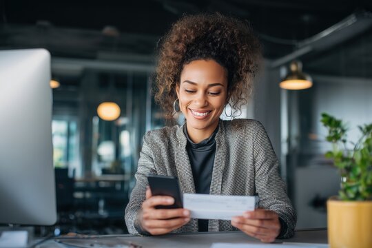 Happy young professional woman looking at her first paycheck and smartphone screen with joy smiling female employee celebrating first salary deposit in modern office finance and career success concept