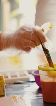 Artist Hand in Glove Dipping Brush into Orange Paint
