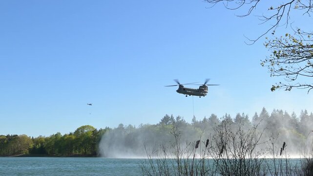 Transport helicopter of Dutch Royal Air Force carrying a water bucket for extinguishing wildfires in nature.