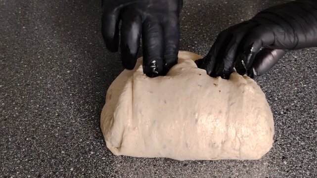 Baker with black gloves kneading and folding sourdough bread dough.
