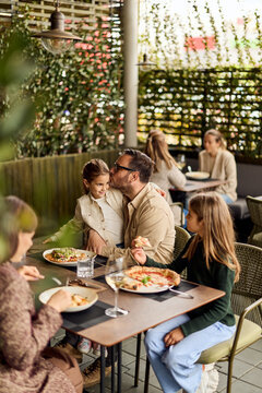 Father Kissing Daughter at Outdoor Family Lunch in Casual Restaurant Patio, Family Bonding Moment