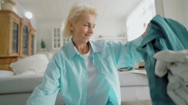 Emotional lady throwing clothes in living room, feel fun and good mood, portrait . Smiling blonde woman sitting alone on floor at home, rejoicing by summer vacation and ability of traveling worldwide
