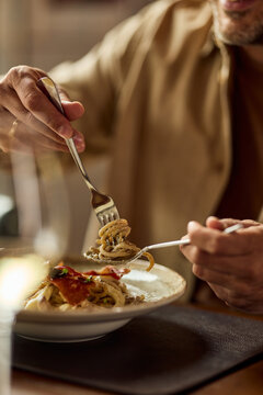 Man Twirling Pasta with Fork in Casual Restaurant Dinner Setting, Enjoying Italian Meal