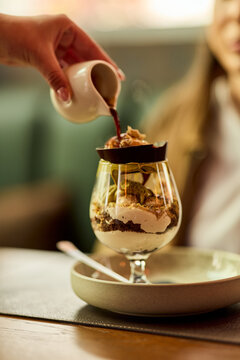 Hand Pouring Espresso Over Gourmet Dessert Parfait In Cozy Cafe With Woman Watching