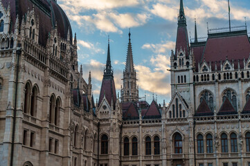 Obraz premium Magnificent view of the Hungarian Parliament Building in Budapest with ornate Gothic Revival architecture and detailed spires under a cloudy evening sky at sunset